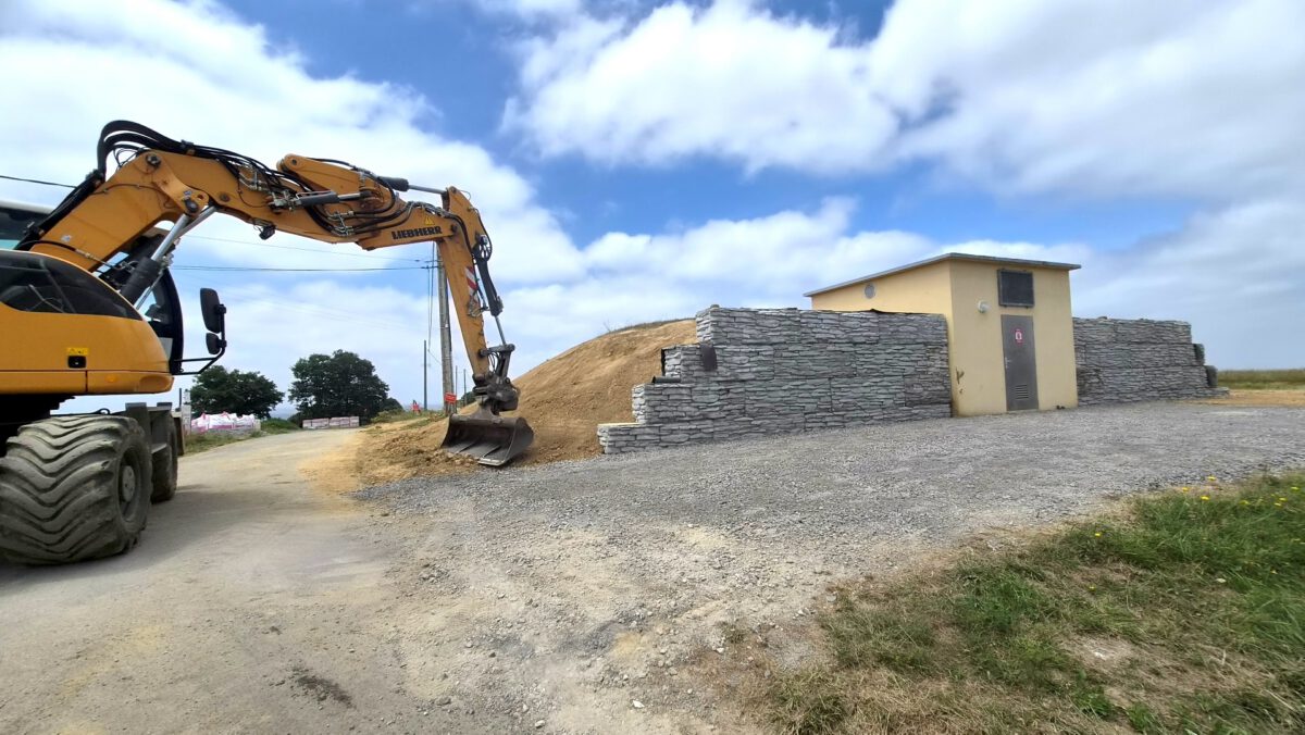 Une pelle mécanique en chantier devant un réservoir, lors de travaux sur le réseau.